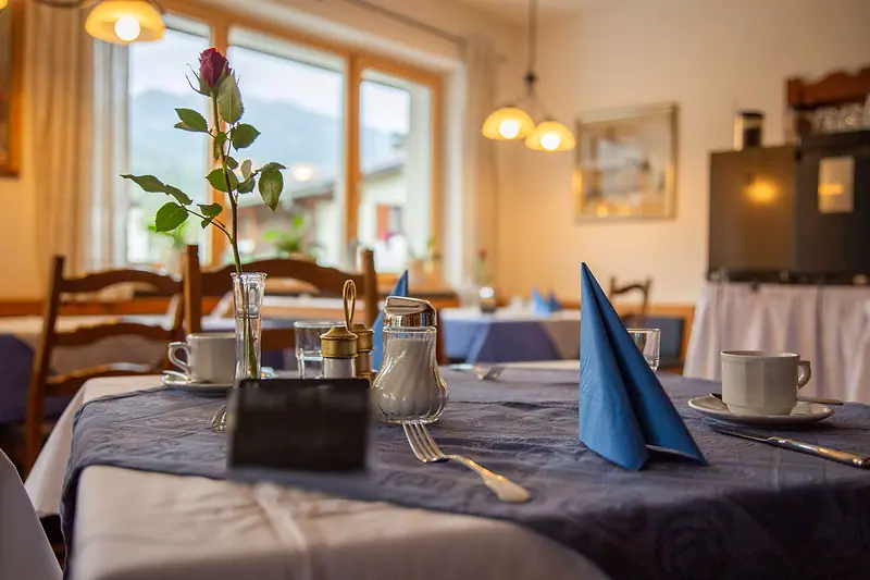 Gedeckter Tisch im Frühstücksraum mit Rose und blauer Serviette