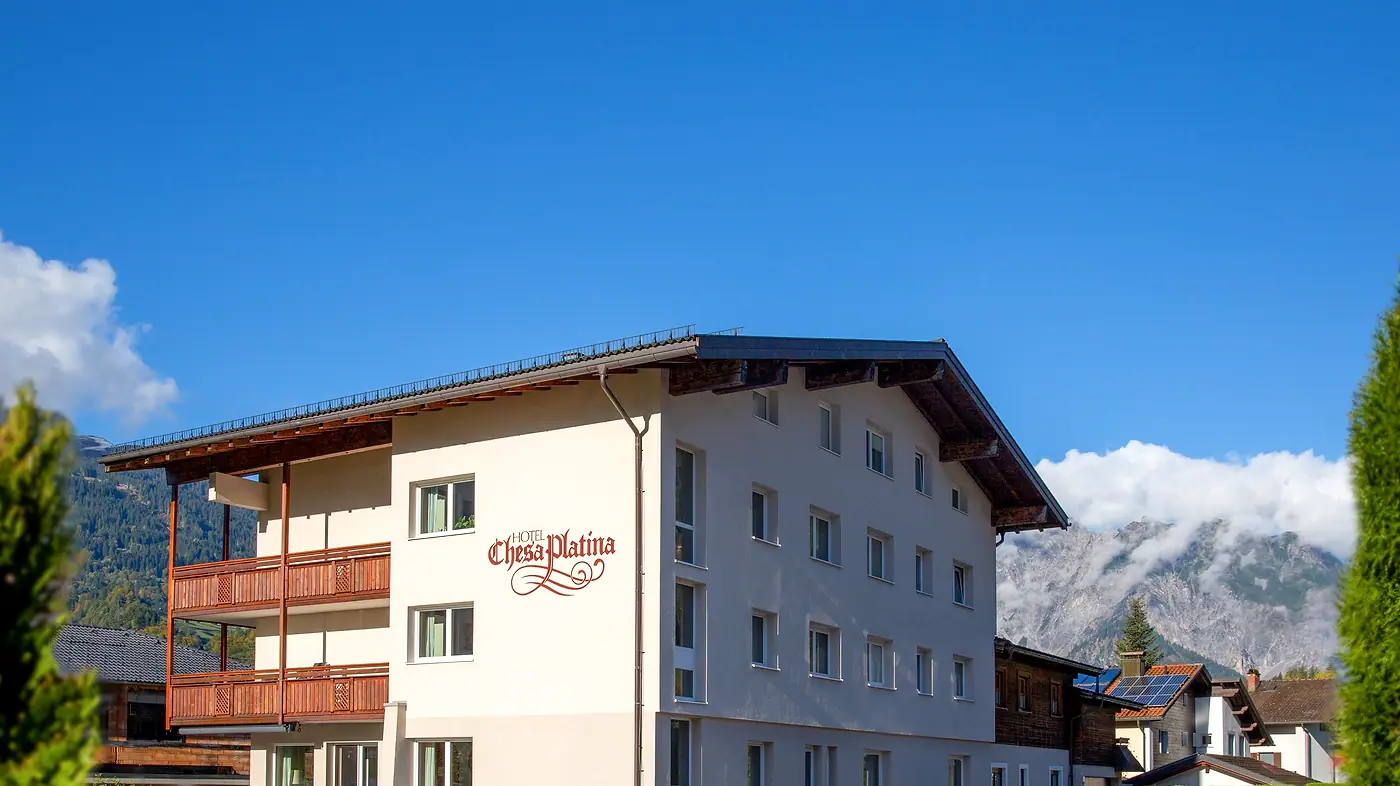 Das Hotel Chesa Platina im Herbst mit Holzbalkonen und Bergen dahinter